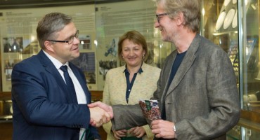 Lietuvos banko valdybos pirmininkas Vitas Vasiliauskas įteikia Vilniui skirtą proginę 2 eurų monetą jos lankstuko autoriui Ernestui Parulskiui